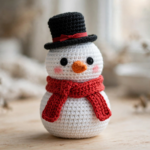 Crochet snowman pattern - finished amigurumi snowman with orange carrot nose, red scarf and black top hat on a wooden table