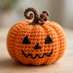 Finished crochet jack-o-lantern amigurumi with black triangle eyes, zigzag smile and curly brown stem on a light wooden table